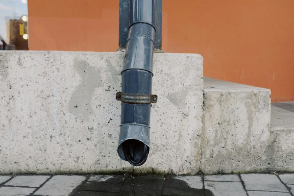 Aged metal drain pipe on a concrete wall with water stains, highlighting urban decay. Tuyau de drainage en métal vieilli sur un mur en béton avec des taches d'eau, mettant en évidence la décadence urbaine.