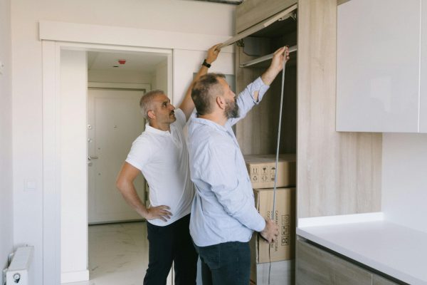 Two men measuring a modern kitchen cabinet for a renovation project in an apartment. Deux hommes mesurant un placard de cuisine moderne pour un projet de rénovation dans un appartement.