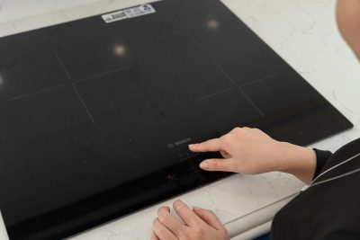 A person interacts with a sleek black induction cooktop in a modern kitchen setting. Une personne interagit avec une plaque de cuisson à induction noire et élégante dans un cadre de cuisine moderne.