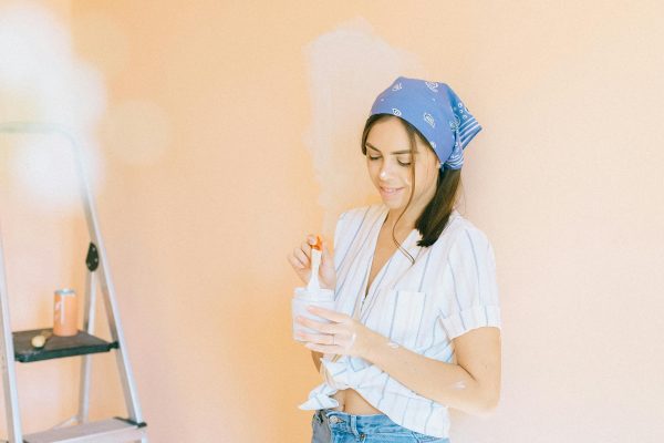 Woman painting a wall with roller, standing beside ladder indoors, home renovation project. Une femme peint un mur avec un rouleau, debout à côté d'une échelle à l'intérieur, projet de rénovation domiciliaire.