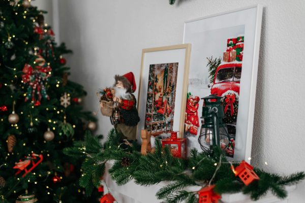 Cozy Christmas mantel with festive decorations, framed art and a holiday tree. Manteau de cheminée confortable pour Noël avec des décorations festives, de l'art encadré et un sapin des fêtes.