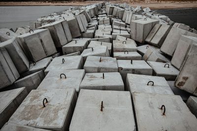 Stacked concrete blocks line a beach under an overcast sky, suggesting a moody atmosphere. Des blocs de béton empilés bordent une plage sous un ciel couvert, suggérant une atmosphère morose.