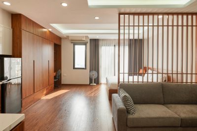Spacious minimalist apartment with wooden accents, featuring sofa, bed, and ceiling lights in Hanoi. Appartement minimaliste spacieux avec des accents en bois, présentant un canapé, un lit et des luminaires au plafond à Hanoï.