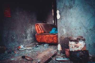 A decaying interior featuring an old leather sofa with debris scattered on the floor. Intérieur en décadence avec un vieux canapé en cuir et des débris éparpillés sur le sol.