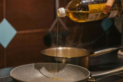 Close-up of hand pouring cooking oil into frying pan during food preparation. Gros plan d'une main versant de l'huile de cuisson dans une poêle à frire pendant la préparation des aliments.