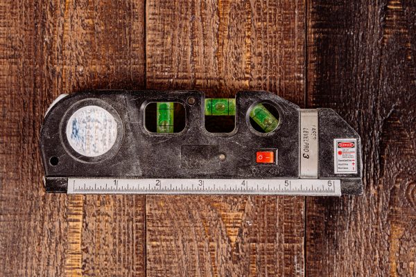 Close-up of a multipurpose laser level tool on a wooden table surface. Gros plan d'un outil de niveau laser polyvalent sur une surface de table en bois.