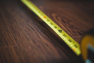 Yellow tape measure extended across a dark wooden floor, highlighting measurement details. Un mètre ruban jaune étendu sur un plancher en bois foncé, mettant en évidence les détails de mesure.