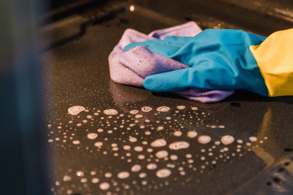 A gloved hand cleans an oven interior using a soapy cloth for a spotless finish. Une main gantée nettoie l'intérieur d'un four avec un chiffon savonneux pour une finition impeccable.