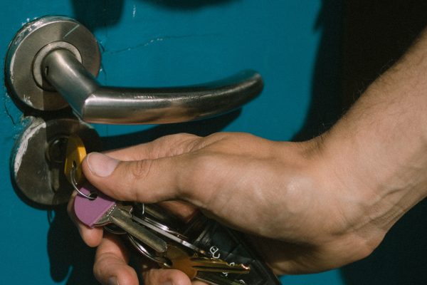 A hand using keys to unlock a vibrant blue door with a metal handle. Une main utilisant des clés pour déverrouiller une porte bleue vibrante avec une poignée métallique.