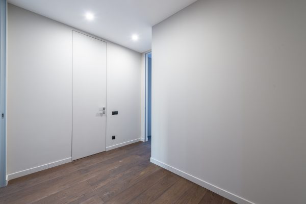 A minimalist indoor corridor featuring sleek doors and wooden flooring under bright lighting. Un couloir intérieur minimaliste présentant des portes épurées et un revêtement de sol en bois sous un éclairage brillant.