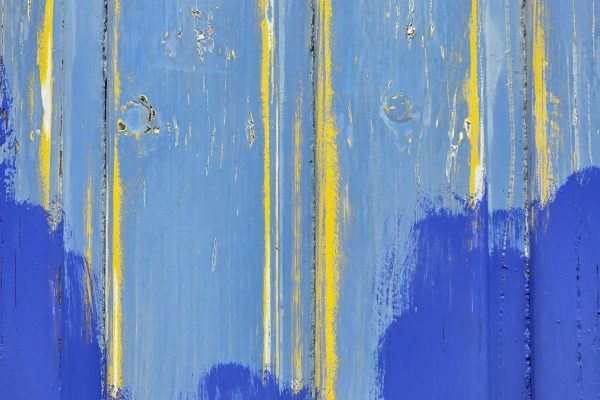 Close-up of blue and yellow paint on a wooden surface creating an abstract pattern. Gros plan de peinture bleue et jaune sur une surface en bois créant un motif abstrait.
