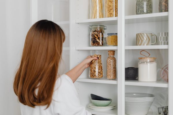 Woman arranging jars on pantry shelves for organized food storage. Une femme arrange des bocaux sur les étagères du garde-manger pour un rangement alimentaire organisé.
