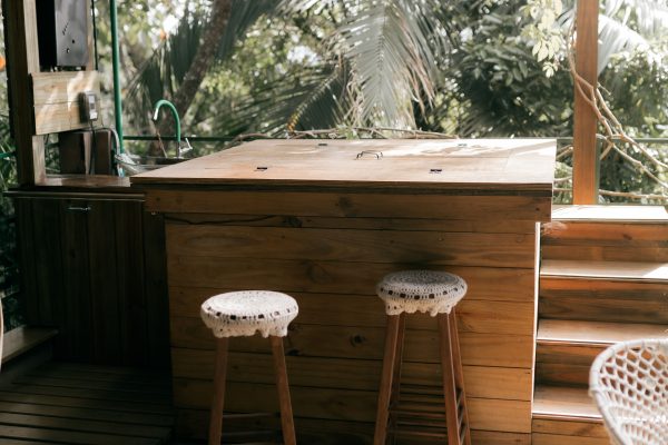 Charming outdoor bar with wooden stools and lush greenery, perfect for relaxation. Un bar extérieur charmant avec des tabourets en bois et une verdure luxuriante, parfait pour se détendre.