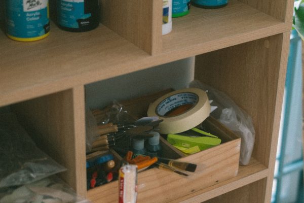 Wooden shelves filled with various art supplies and tools in an indoor setting. Des étagères en bois remplies de diverses fournitures artistiques et d'outils dans un cadre intérieur.