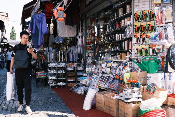 Man browsing tools at a vibrant outdoor market stall offering diverse hardware products. Un homme parcourant des outils à un étal de marché extérieur vibrant offrant divers produits de quincaillerie.