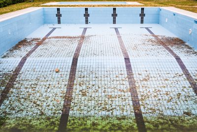 High angle view of an empty, abandoned swimming pool with leaves scattered on the tiled surface. Vue de haut d'une piscine abandonnée et vide avec des feuilles éparpillées sur la surface carrelée.