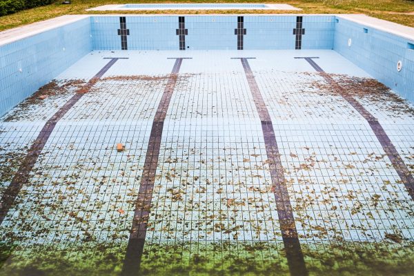 High angle view of an empty, abandoned swimming pool with leaves scattered on the tiled surface. Vue de haut d'une piscine abandonnée et vide avec des feuilles éparpillées sur la surface carrelée.