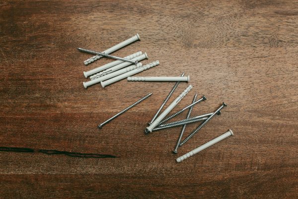 Close-up of screws and nylon anchors laid on a wooden background. Gros plan de vis et chevilles en nylon posées sur un fond en bois.