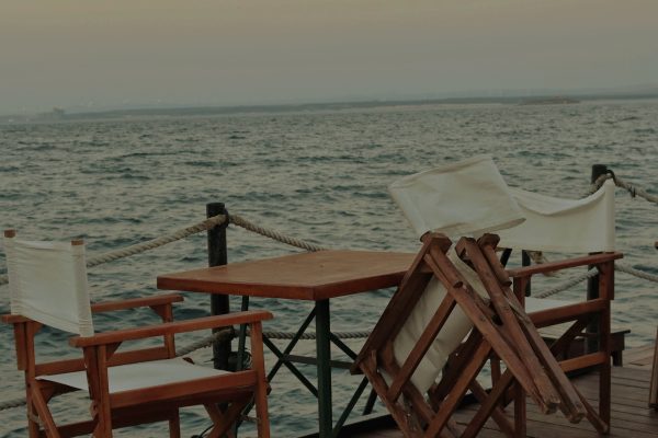 Tranquil seaside deck setup with wooden chairs and a table overlooking the ocean. Configuration tranquille de terrasse bord de mer avec des chaises en bois et une table donnant sur l'océan.